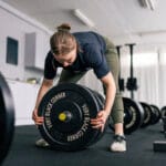 Nainen lastaa levypainoja tankoon maastavetoa varten kuntosalilla. Voimaharjoittelu kuormittaa kehoa hallitusti ja kehittää toimintakykyä.